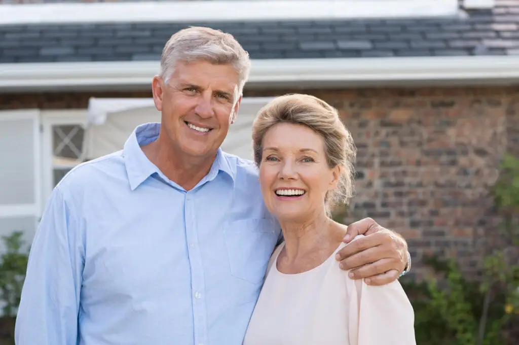 Senior couple smiling outside a brick house, representing senior living in Oklahoma.